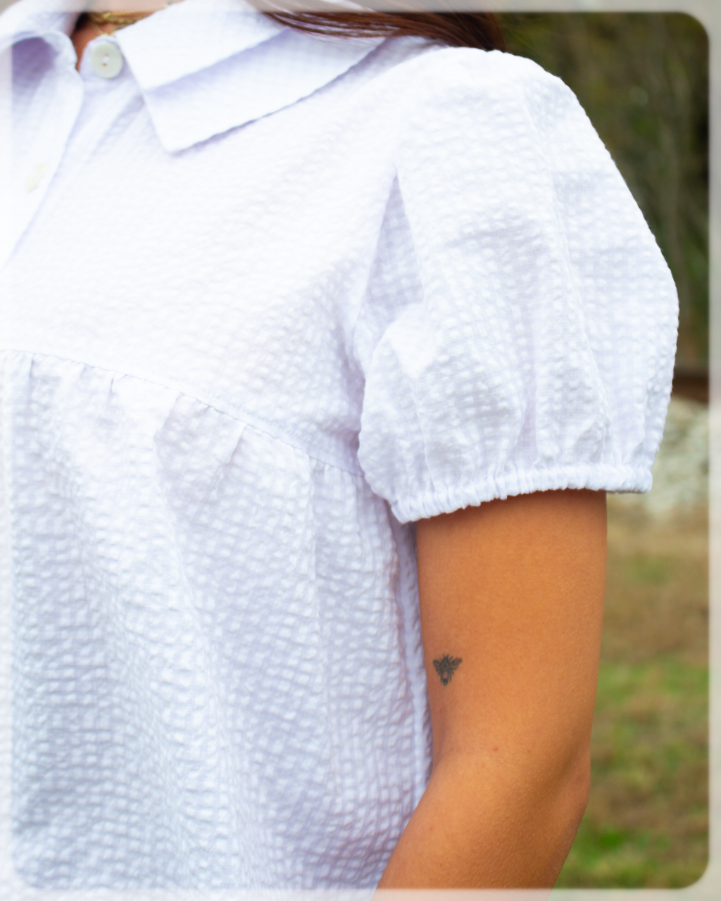 White button up collared textured blouse with puff short sleeves worn by a person outdoors.