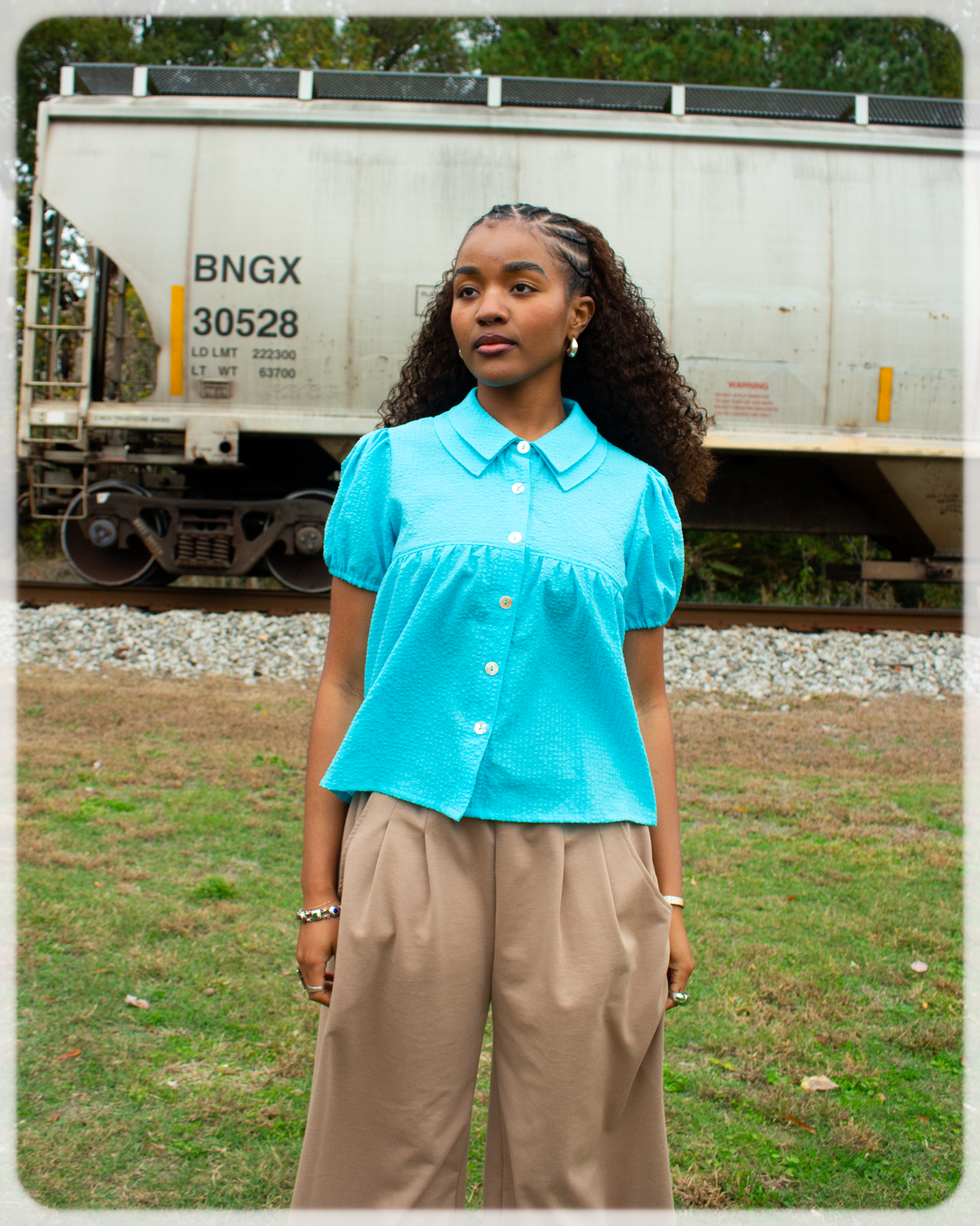 Woman in a Bright Cerulean blue shirt and beige pants standing in front of a train car.