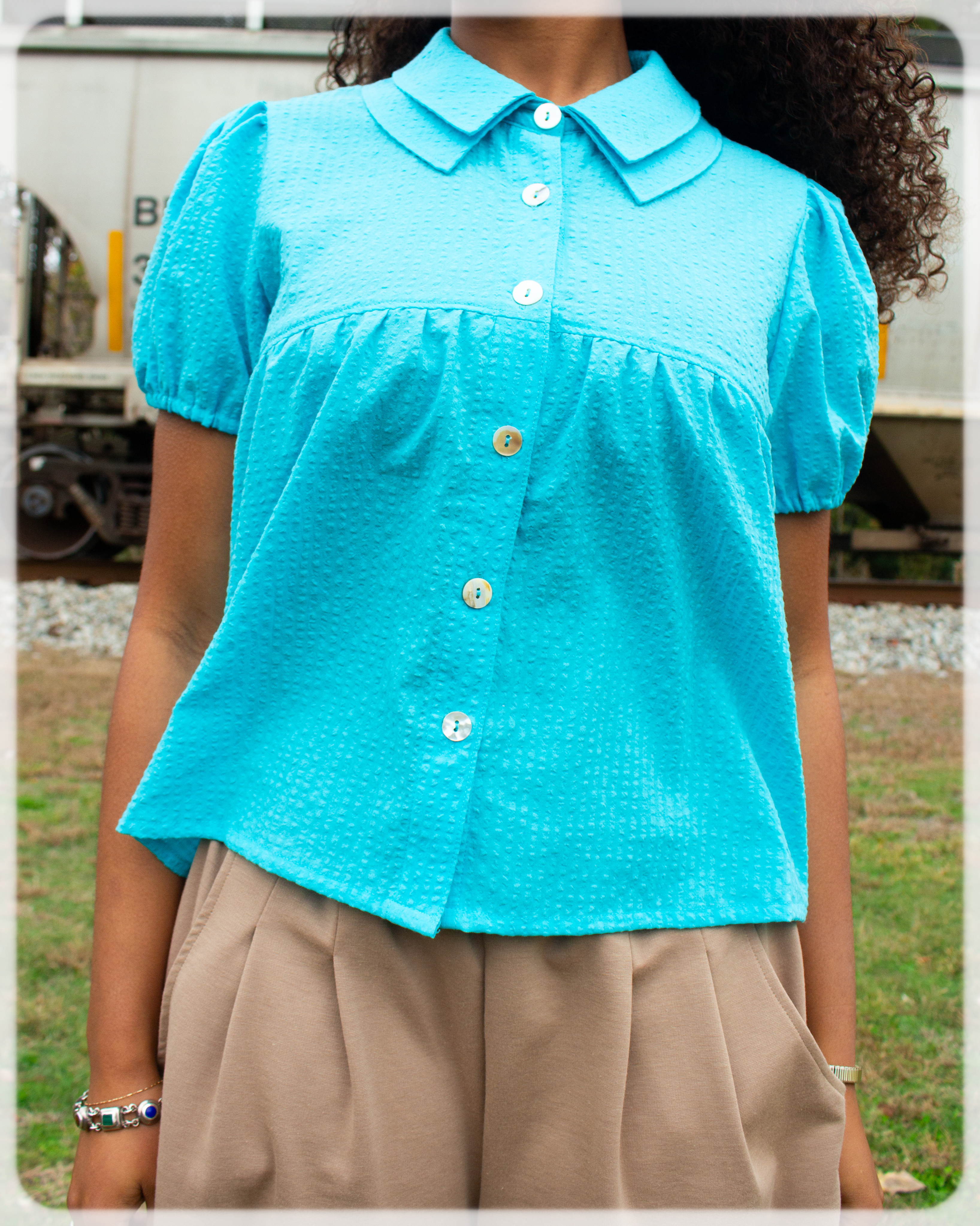 Person wearing a Bright Cerulean blue turquoise blouse with a blurred outdoor background 